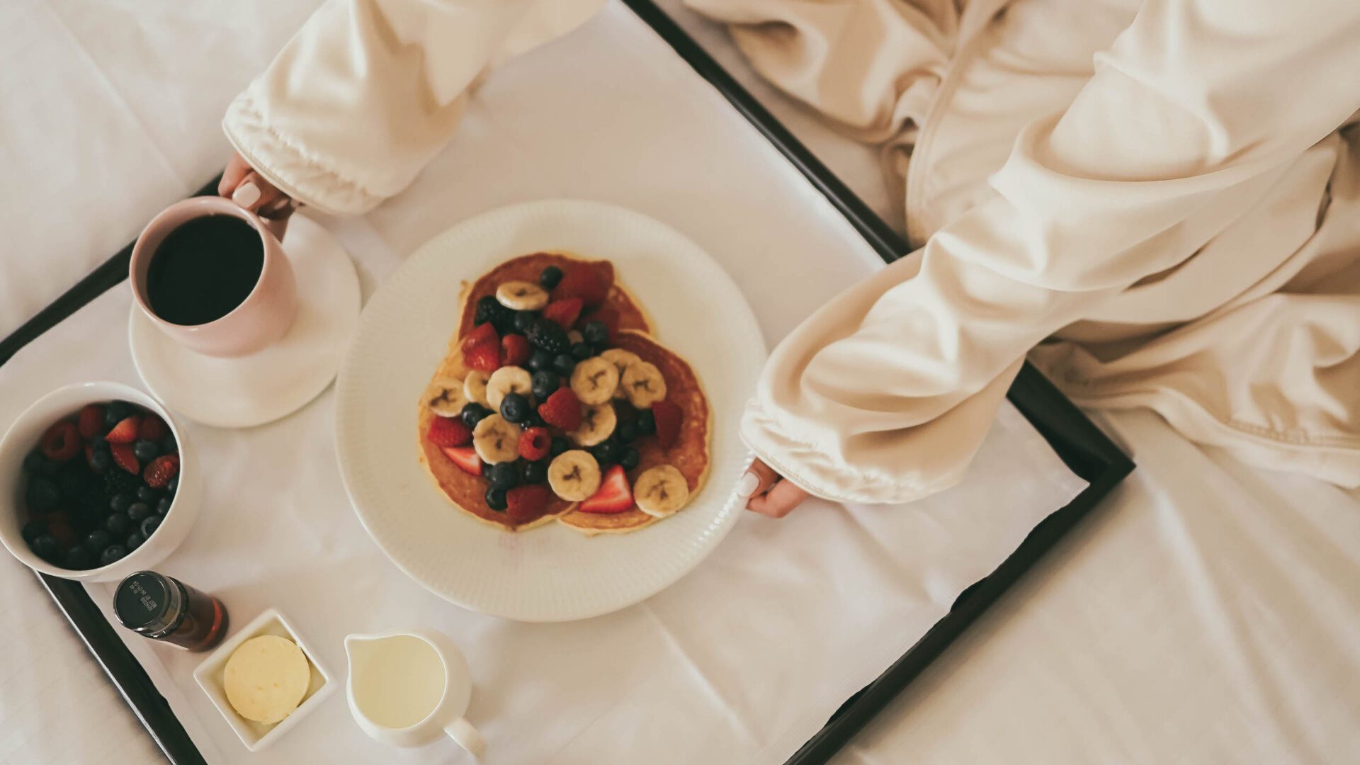 woman enjoying a tray of pancakes with berries while in bed