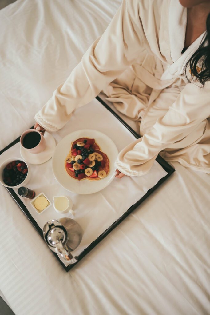 woman enjoying a tray of pancakes with berries while in bed